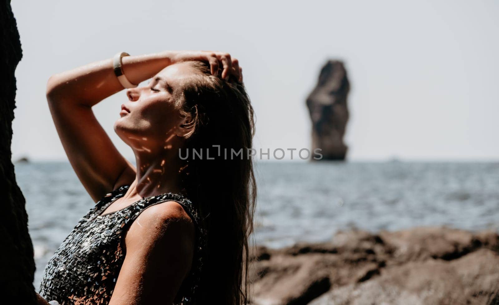 Woman travel sea. Young Happy woman in a long red dress posing on a beach near the sea on background of volcanic rocks, like in Iceland, sharing travel adventure journey