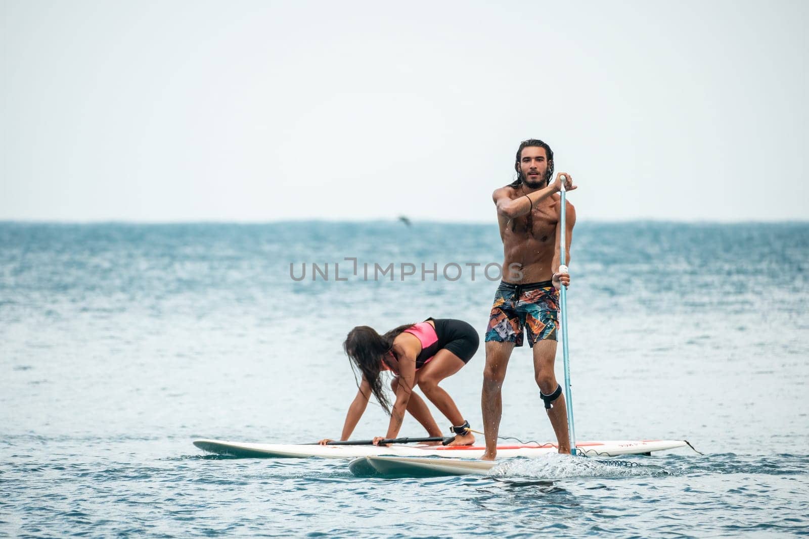 Sea woman and man on sup. Silhouette of happy young woman and man, surfing on SUP board, confident paddling through water surface. Idyllic sunset. Active lifestyle at sea or river