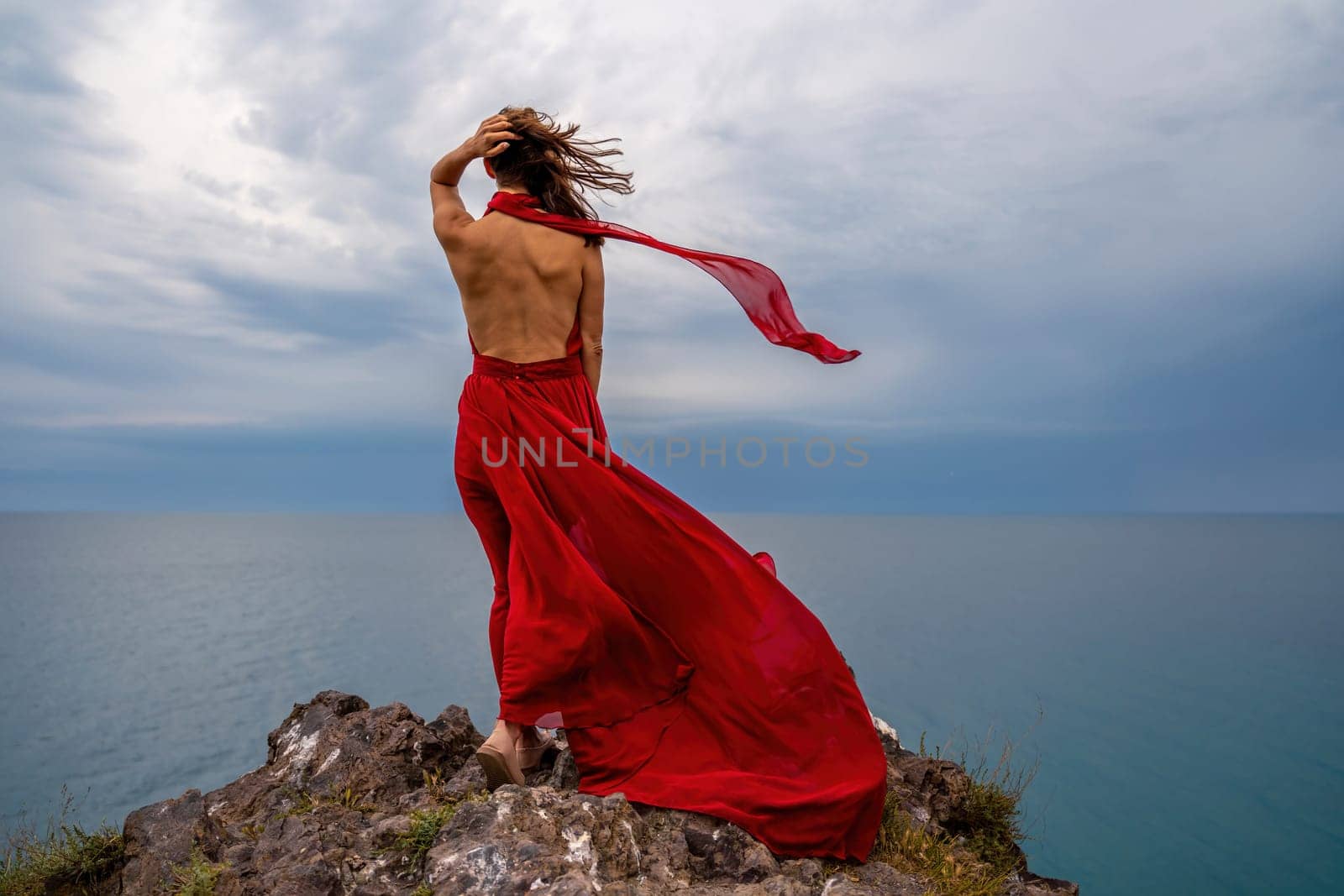 A woman in a red dress stands above a stormy sky, her dress fluttering, the fabric flying in the wind. by Matiunina