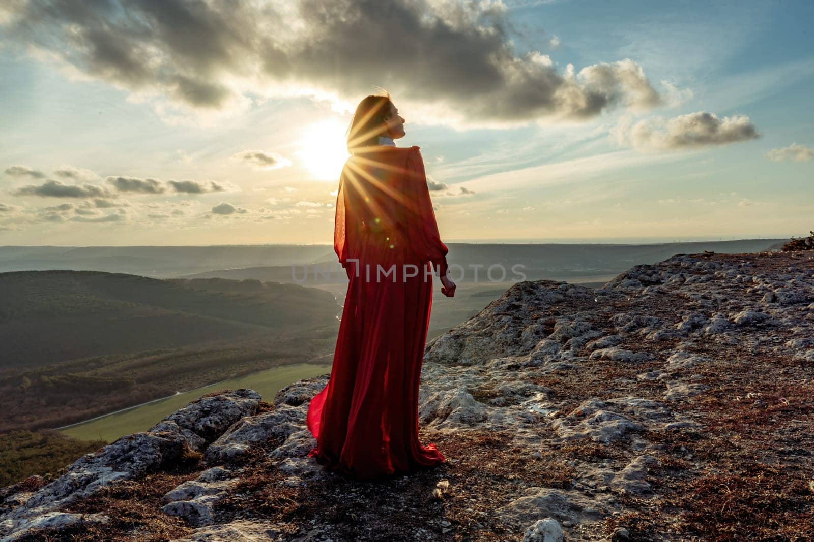 Rise of the mystic. sunset over the clouds with a girl in a long red dress. Stands on the mountain with a magical view