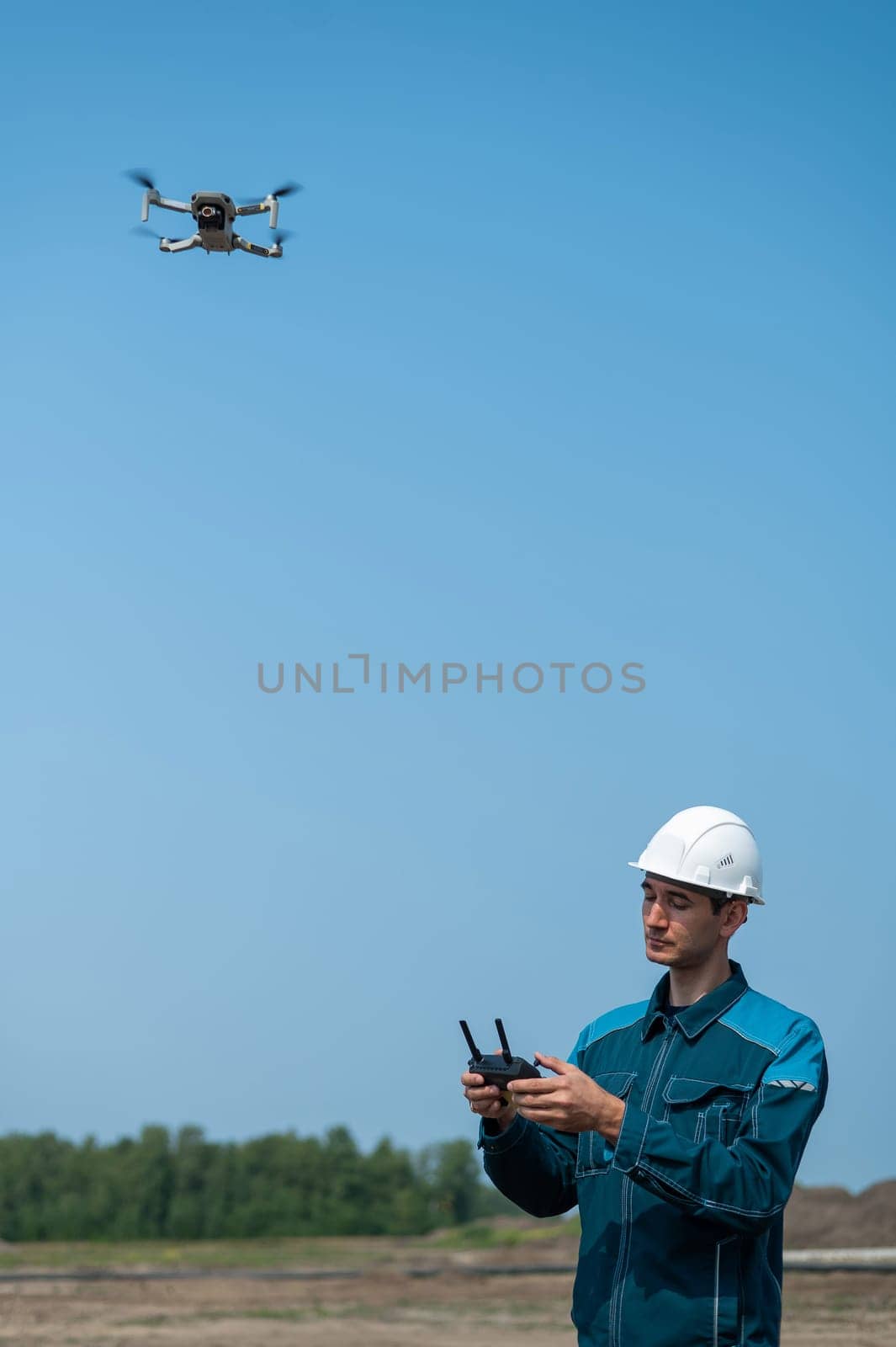 A man in a helmet and overalls controls a drone at a construction site. The builder carries out technical oversight. by mrwed54