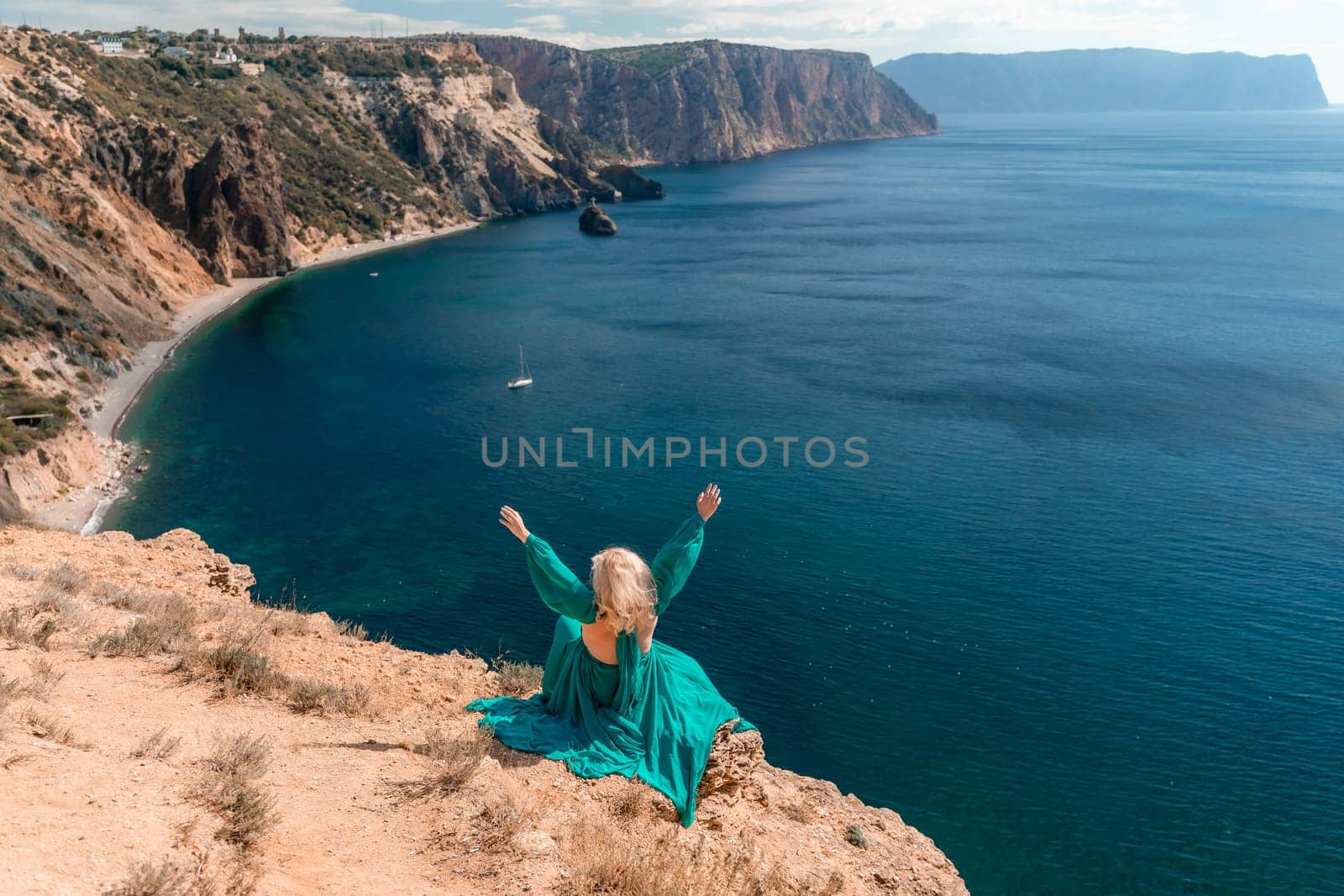 Woman sea. A happy girl is sitting with her back to the viewer in a mint dress on top of a mountain against the background of the ocean and rocks in the sea