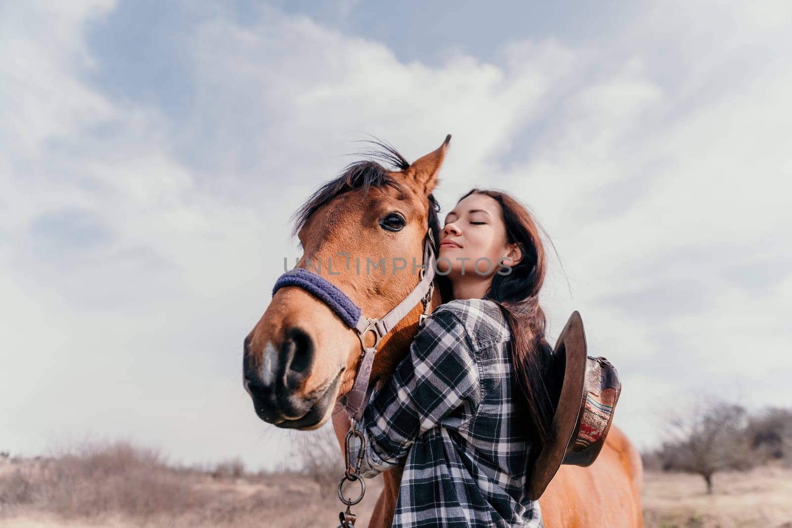 Cute happy young woman with horse. Rider female drives her horse in nature on evening sunset light background. Concept of outdoor riding, sports and recreation.