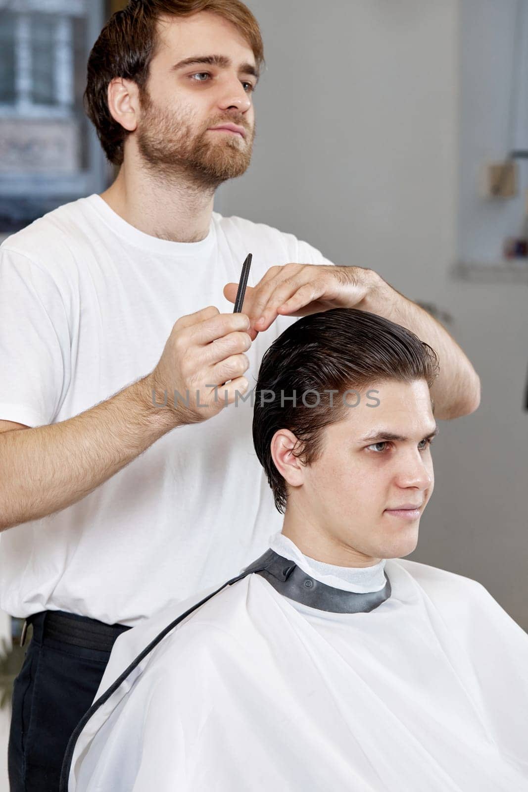 Barber talking to caucasian man while sitting in chair by erstudio