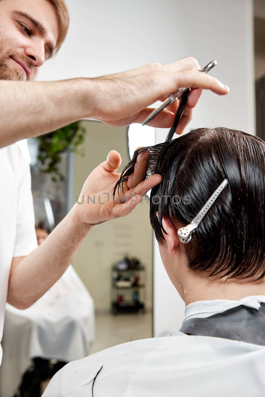 professional male hairstylist serving young caucasian client man at modern barber shop.