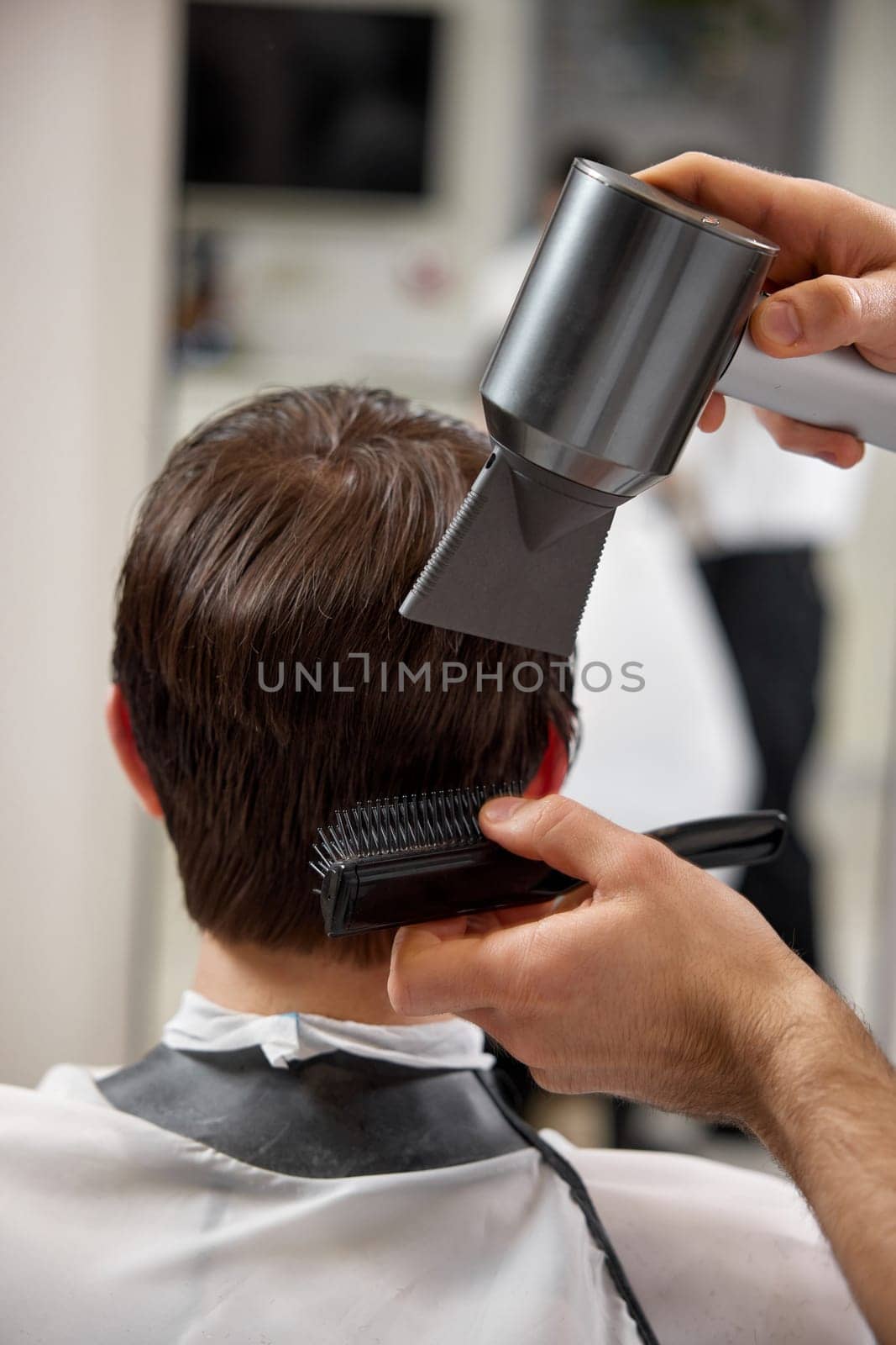 Professional hairdresser during work with man client with hair dryer in barber shop. Haircut in the barbershop.