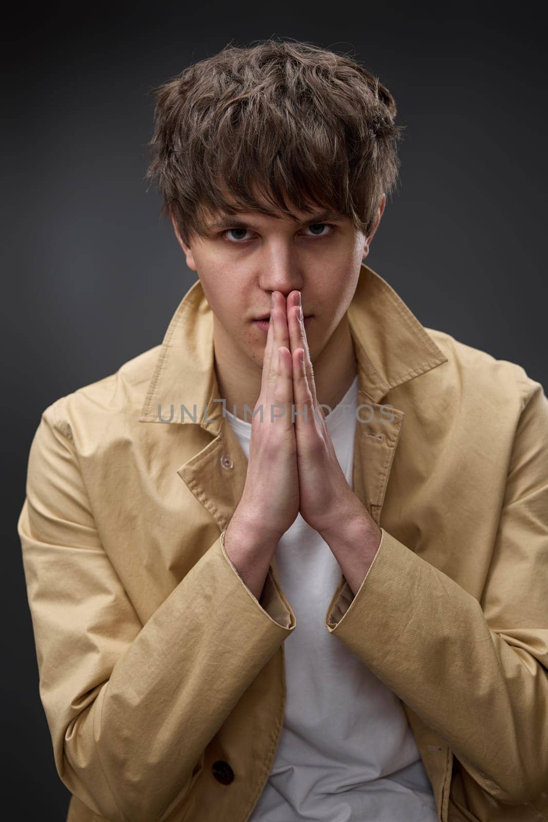 young man in coat holding hands in pray on black background.