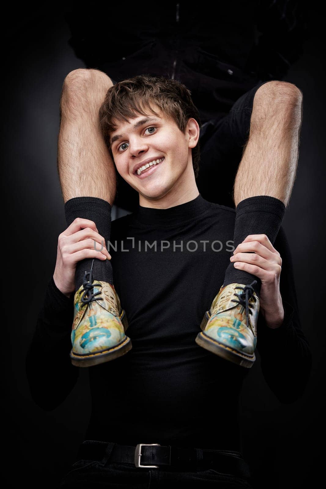 young handsome guy hugs male legs in bright shoes on black background. fashion