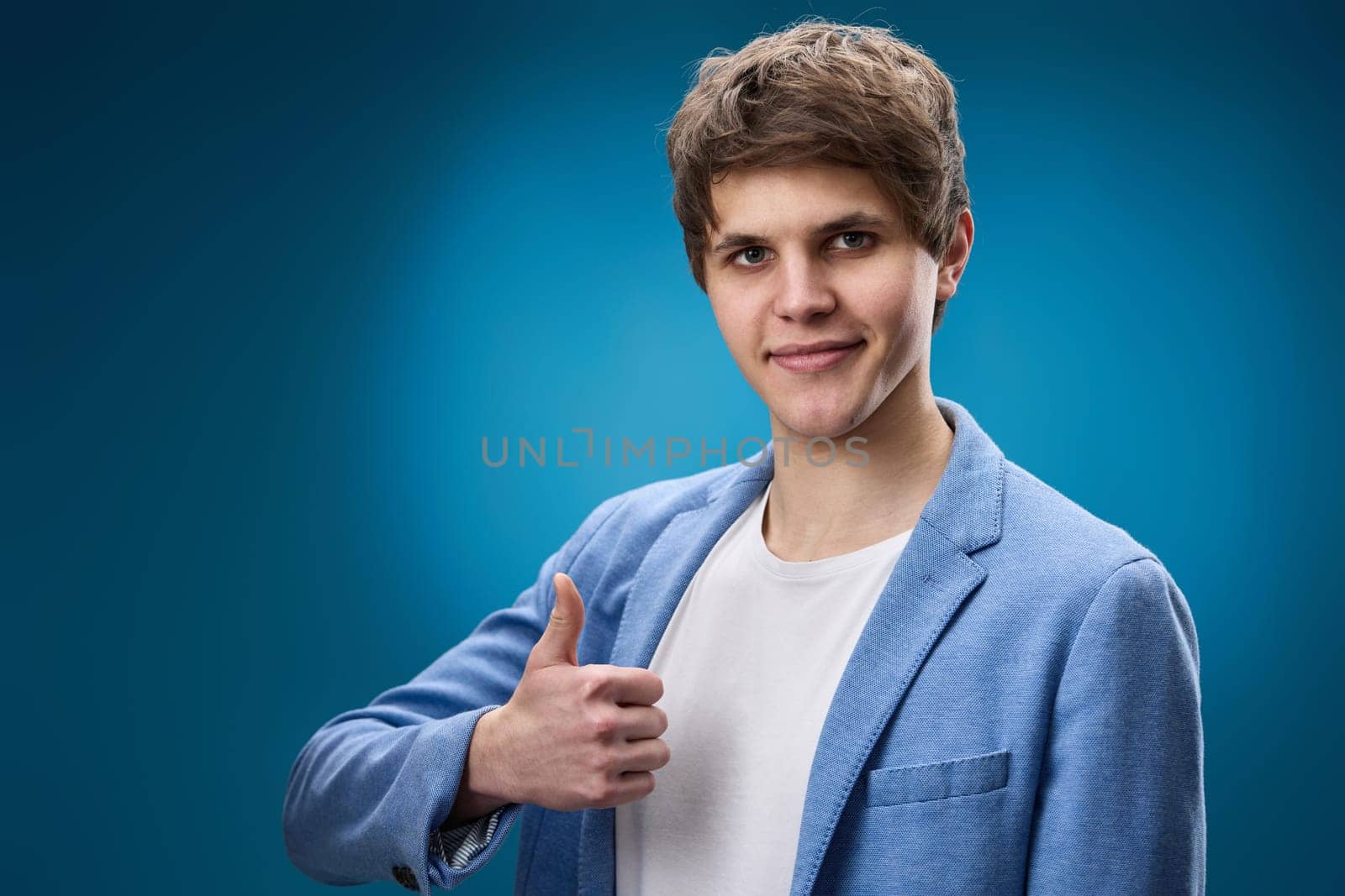 happy young man in jacket showing Ok gesture on blue background.