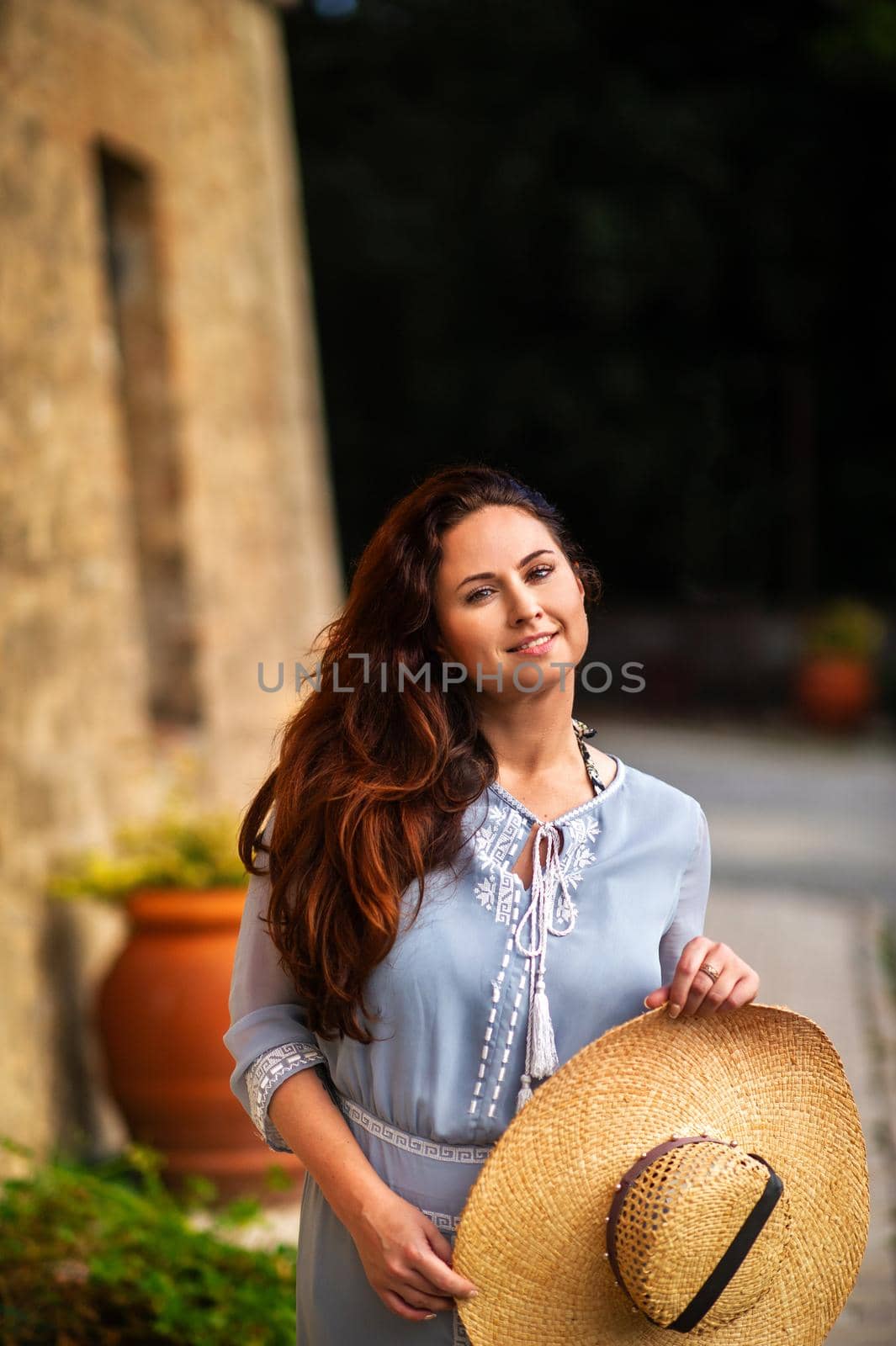 A girl in a dress and hat walks in the afternoon in an Italian town in Tuscany.