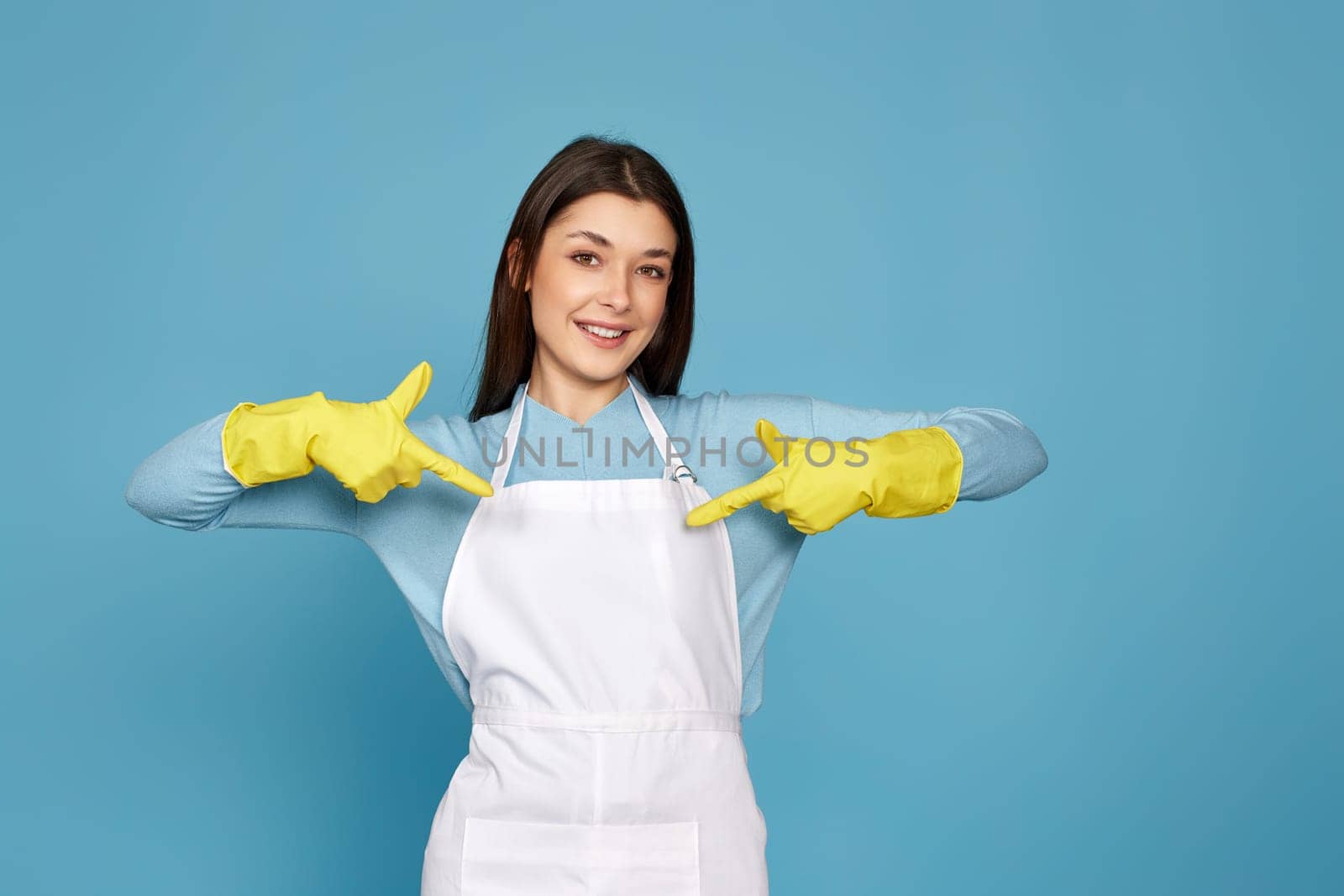 happy caucasian woman in yellow rubber gloves pointing oneself with fingers on blue background. cleaning