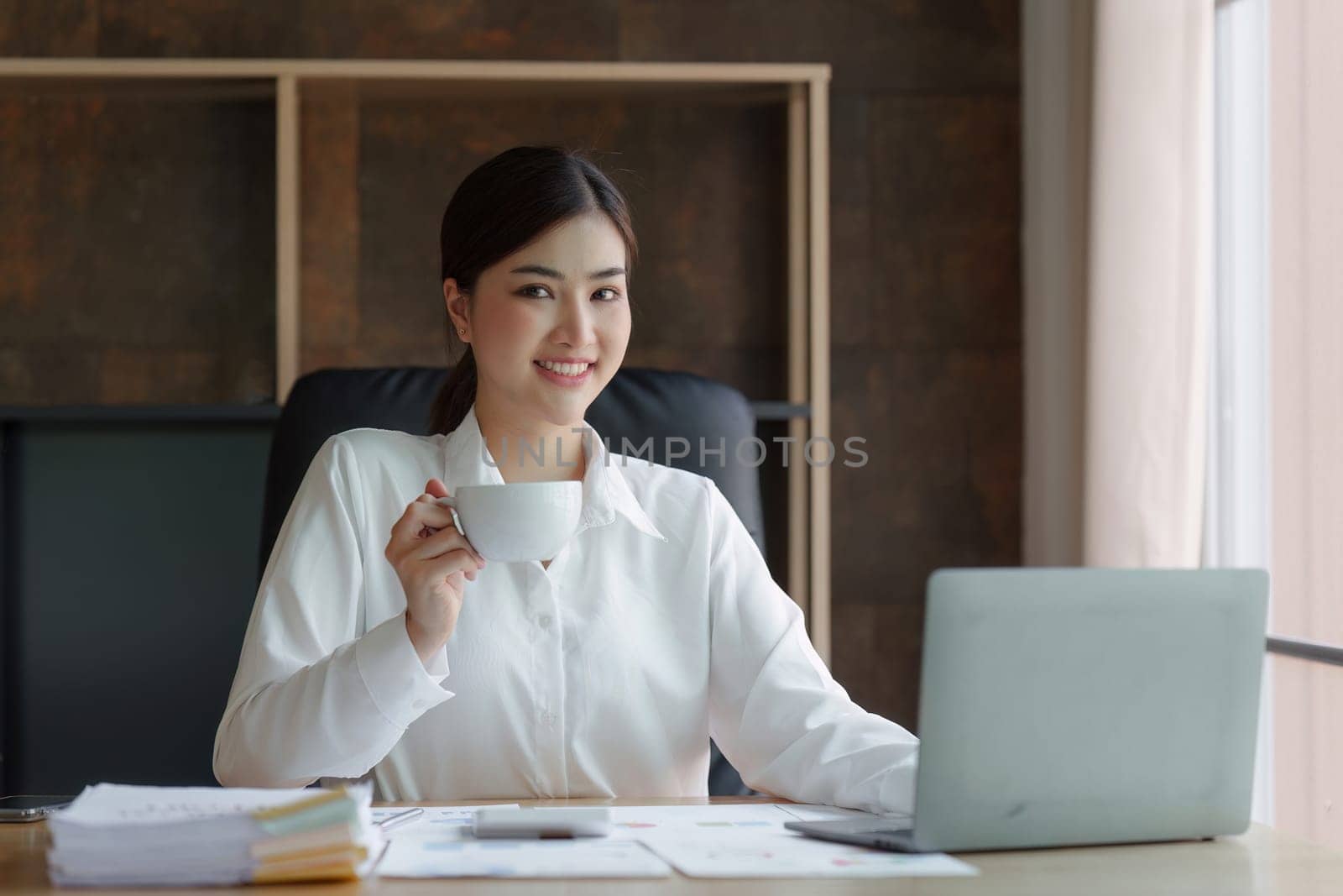 Attractive asian businesswoman sitting and drinking coffee at the desk in home office by itchaznong
