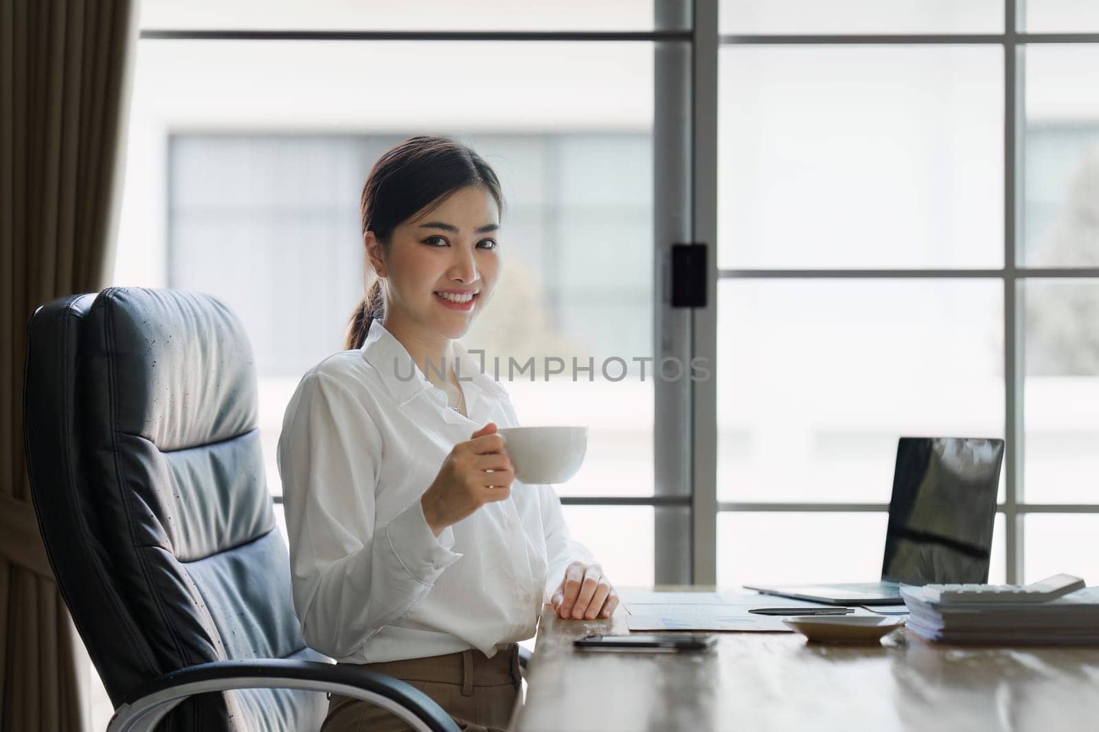 Attractive asian businesswoman sitting and drinking coffee at the desk in home office.