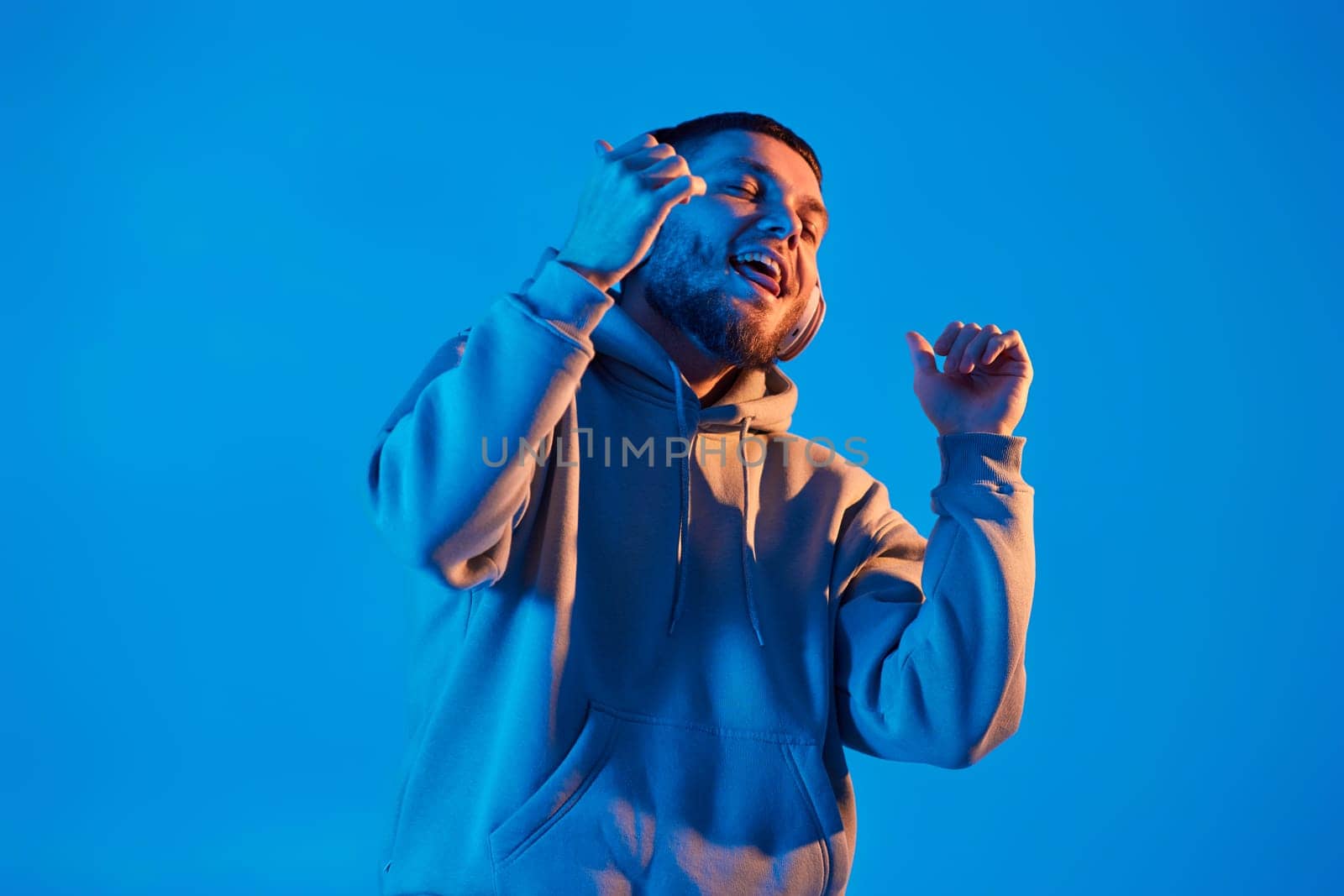 handsome man listening to music with wireless headphones on blue background. Neon lighting