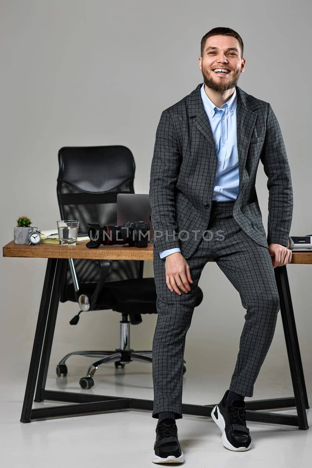successful bearded male photographer smiling cheerfully while working at her desk.