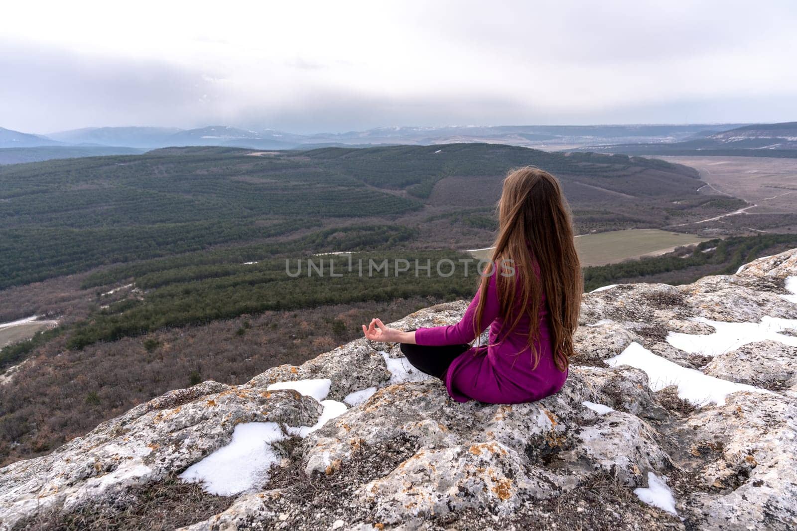 A beautiful woman sits in a lotus position on a high place with an amazing view of the mountains and the gorge practicing yoga meditation Kundalini energy thinking intuition prana. Loneliness harmony mental freedom concept.