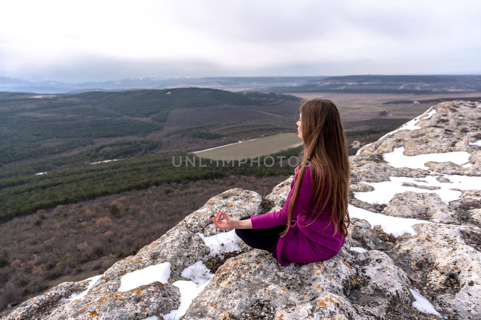 A beautiful woman sits in a lotus position on a high place with an amazing view of the mountains and the gorge practicing yoga meditation Kundalini energy thinking intuition prana. Loneliness harmony mental freedom concept.