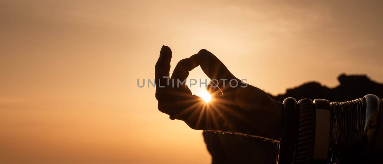 Banner. Young woman's hand in bracelets. Practice yoga on the beach with sunset. Keeps fingers connected, the sun shines through them. The concept of a healthy lifestyle, harmony. by Matiunina