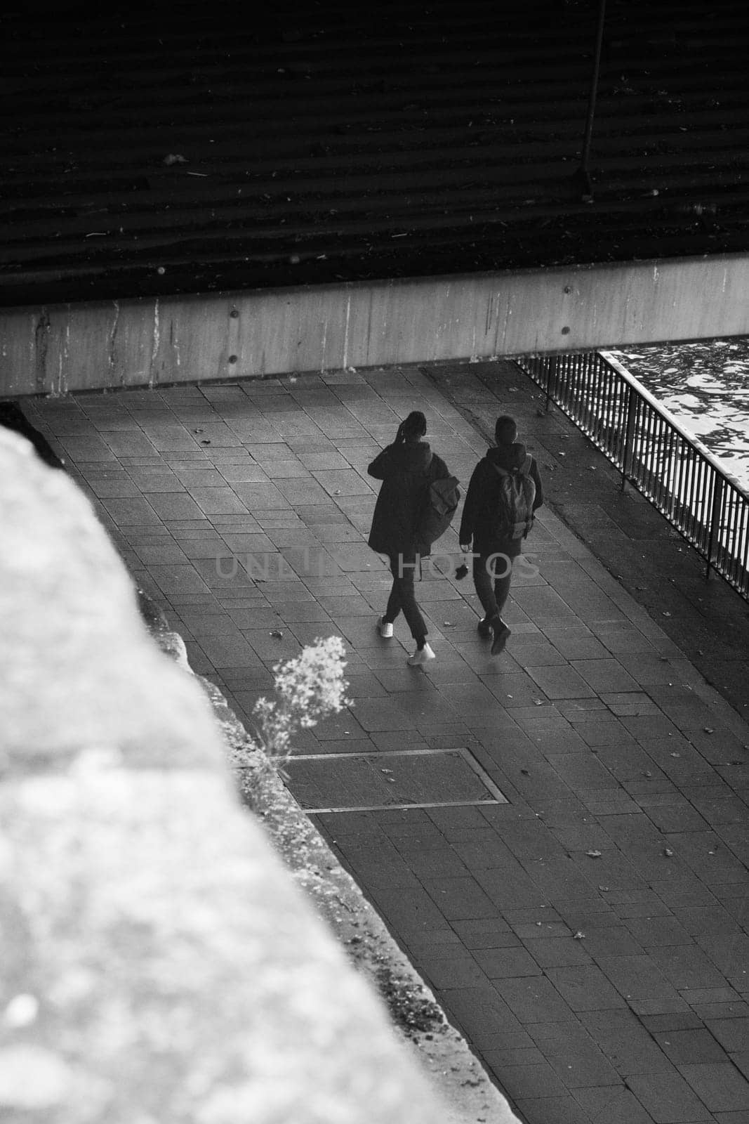Grayscale rooftop view of two people walking under Hohenzollern bridge in Cologne, Germany