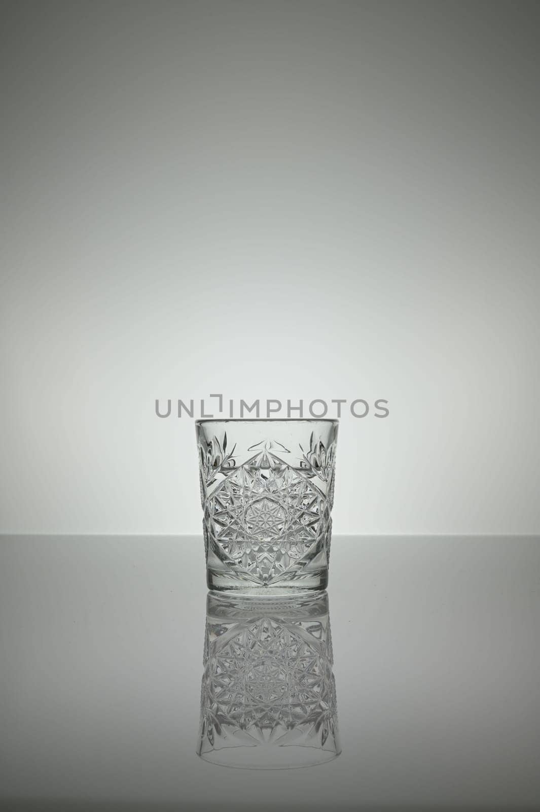 Crystal water glass reflecting on a gray surface with white background