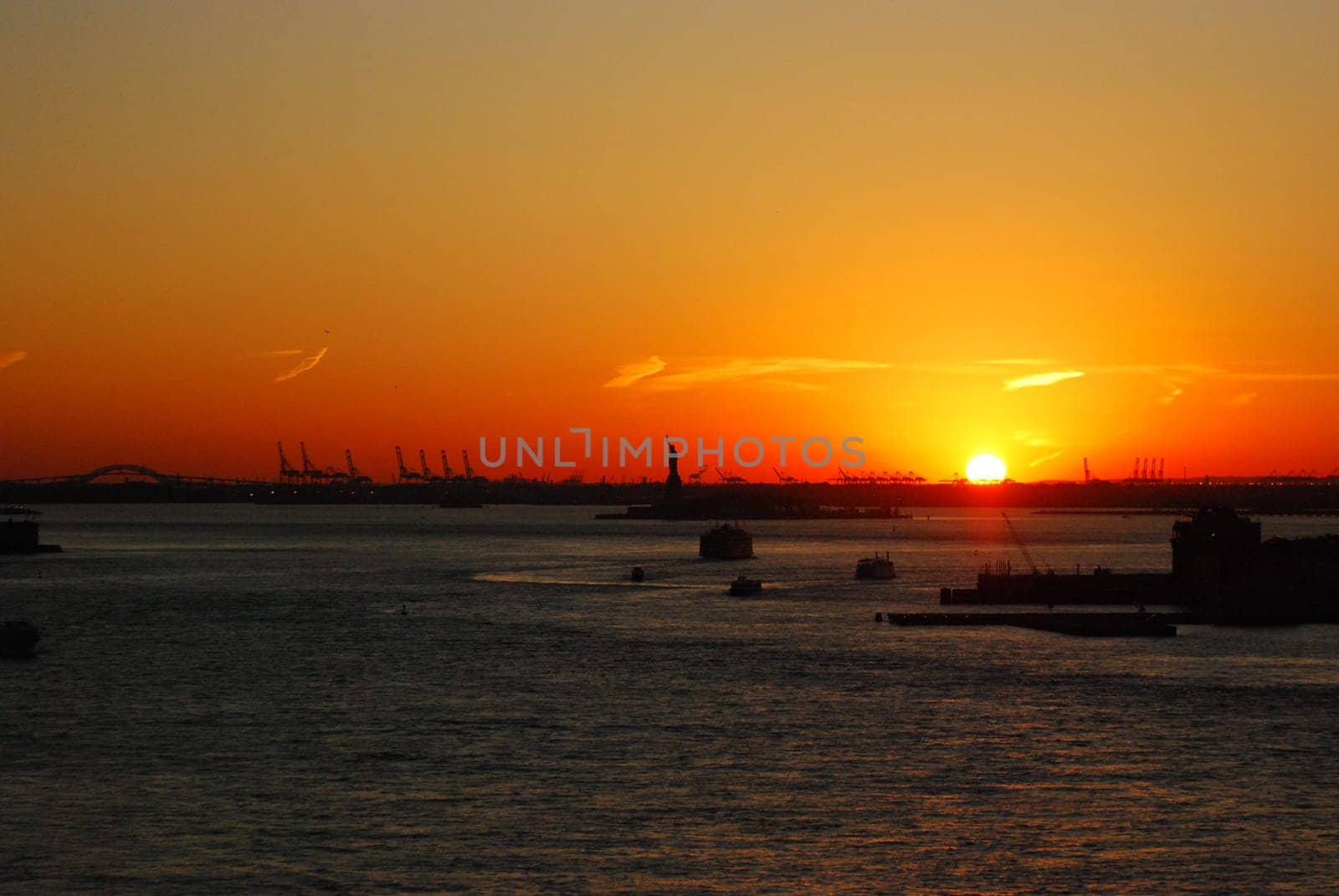 Silhouette of Statue of Liberty and Liberty Island in New York against an orange sunset sky