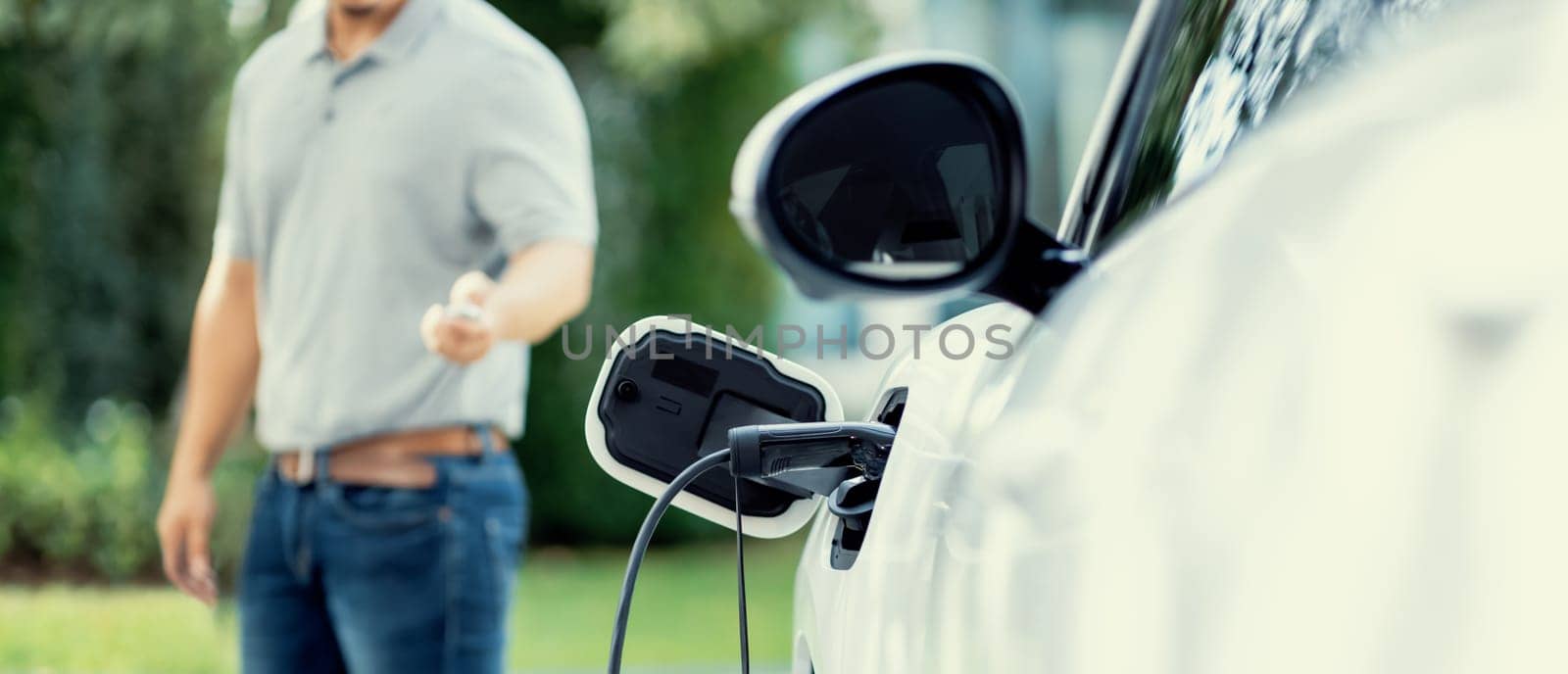Focus recharging electric vehicle outdoor from charging station with blurred background of man at EV car. Concept ideal for new progressive technology of green and renewable energy for car.