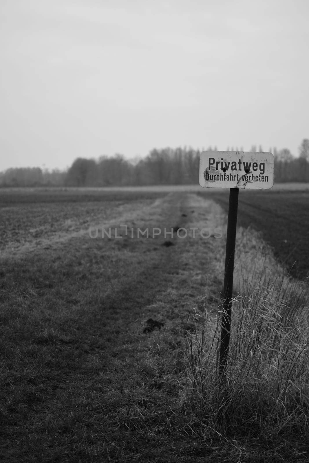 Vertical greyscale shot of a sign showing a private way on a field in Meerbusch, Germany