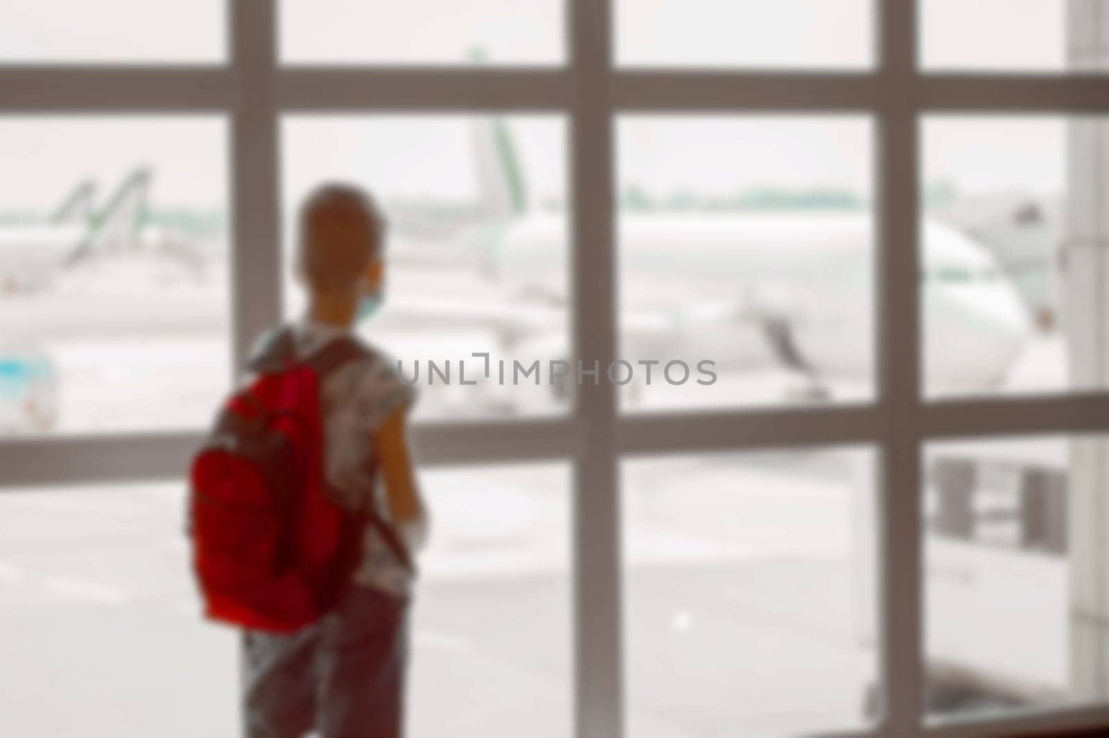 Blurred back view of a boy with red backpack in the waiting room at the airport.