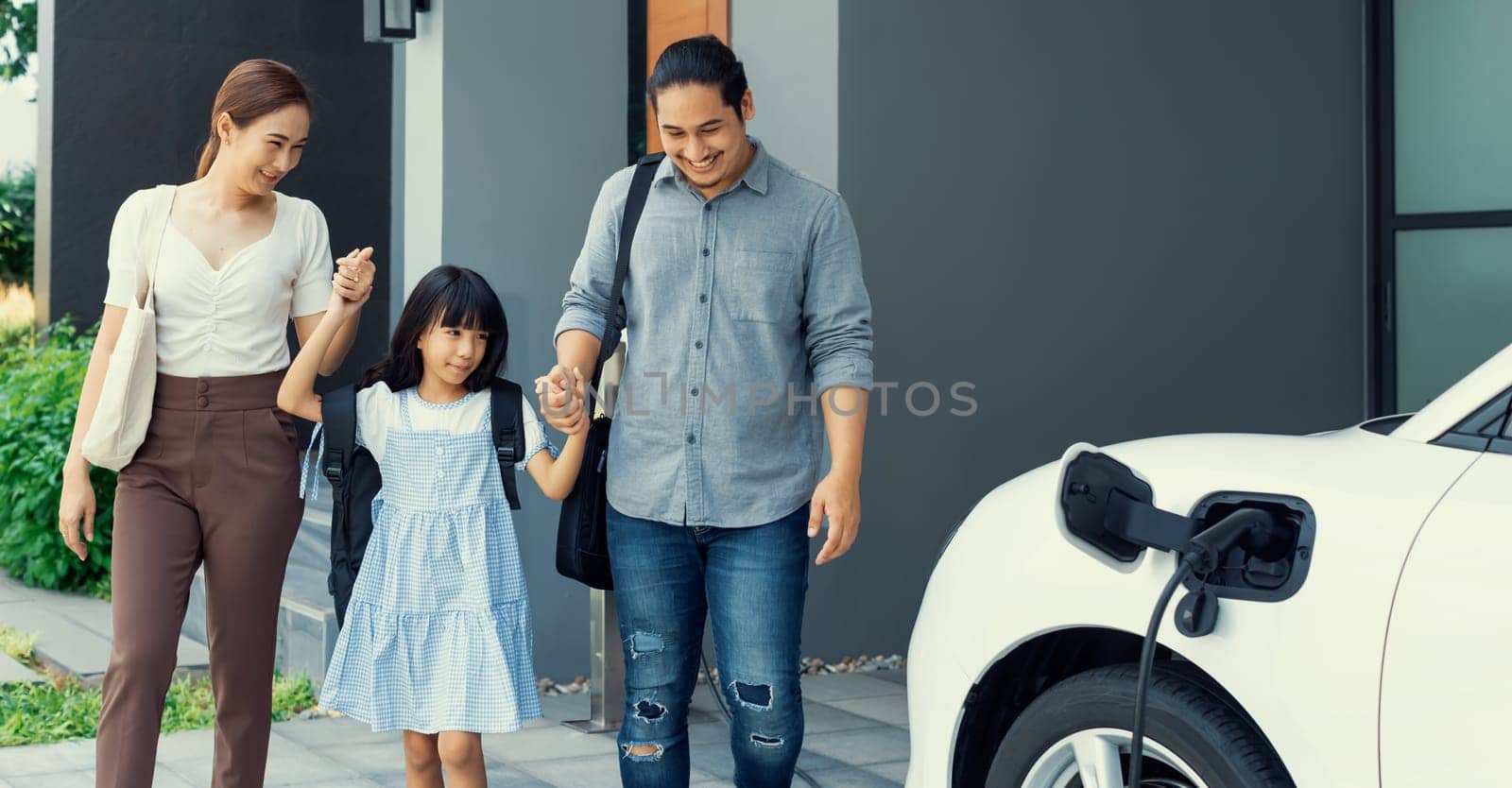 Progressive young parents and daughter living in a home with an electric car. by biancoblue