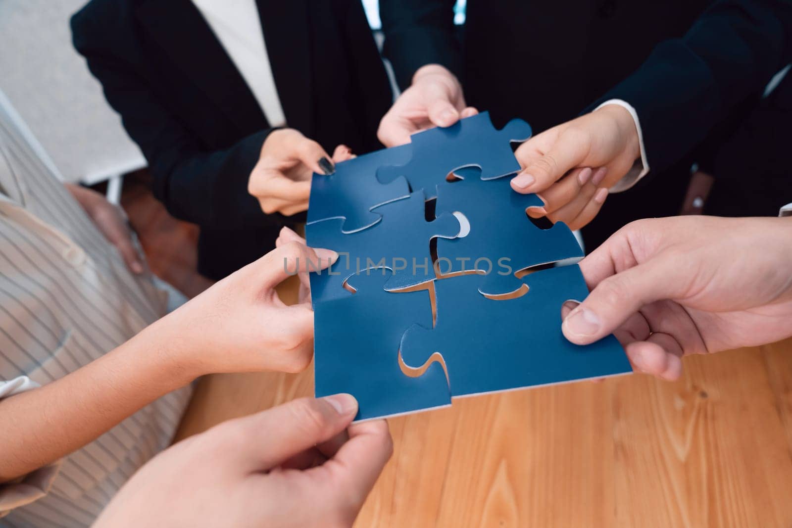 Closeup top view business team of office worker putting jigsaw puzzle together over table filled with financial report paper in workplace with manager to promote harmony concept in meeting room.