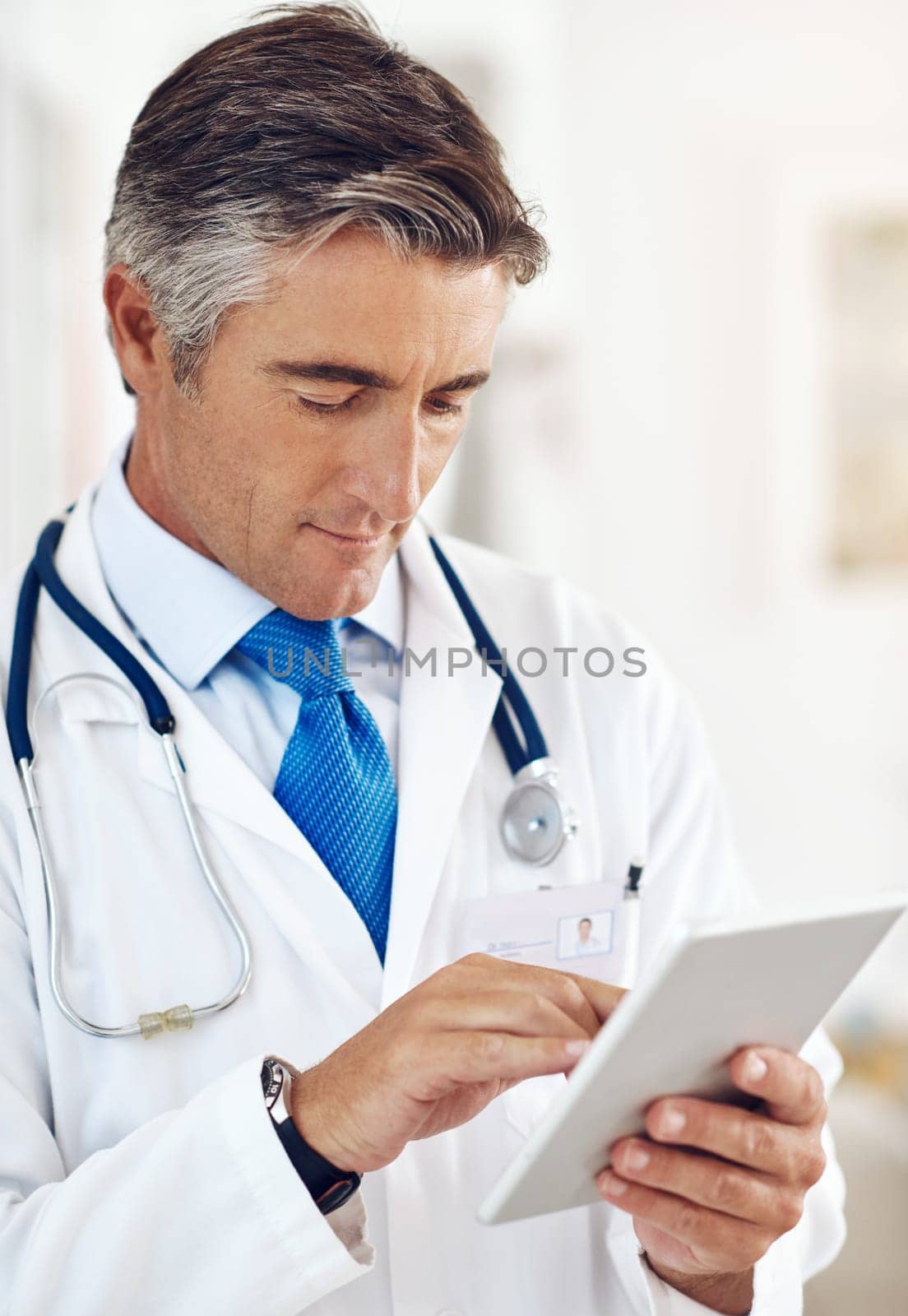 Technology is a great help to him. a handsome mature male doctor holding a digital tablet while standing in a hospital corridor