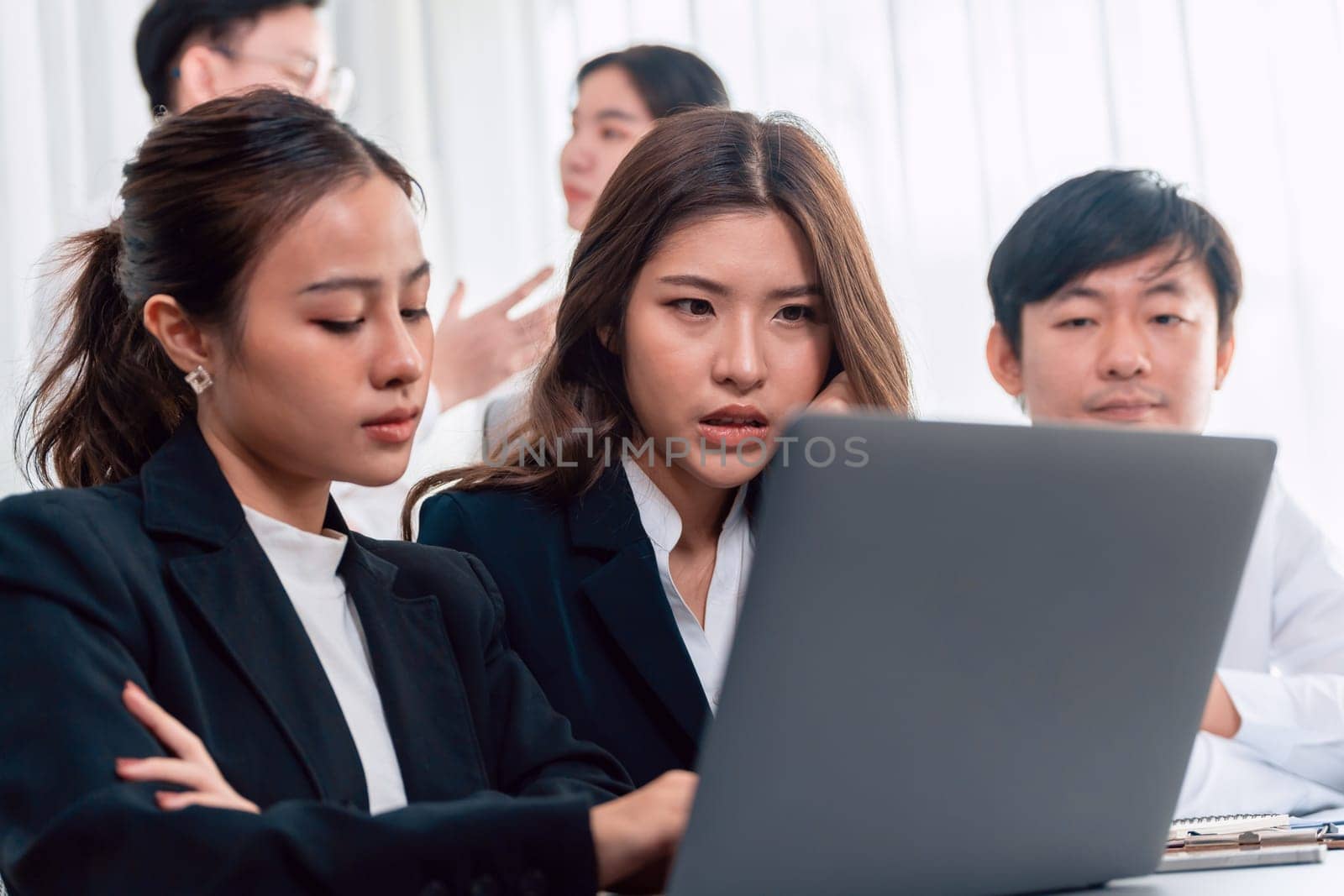 Focused businesspeople using laptop working on data analysis with serious facial expression in corporate environment at harmony office. Struggle in financial strategy planning at meeting desk.