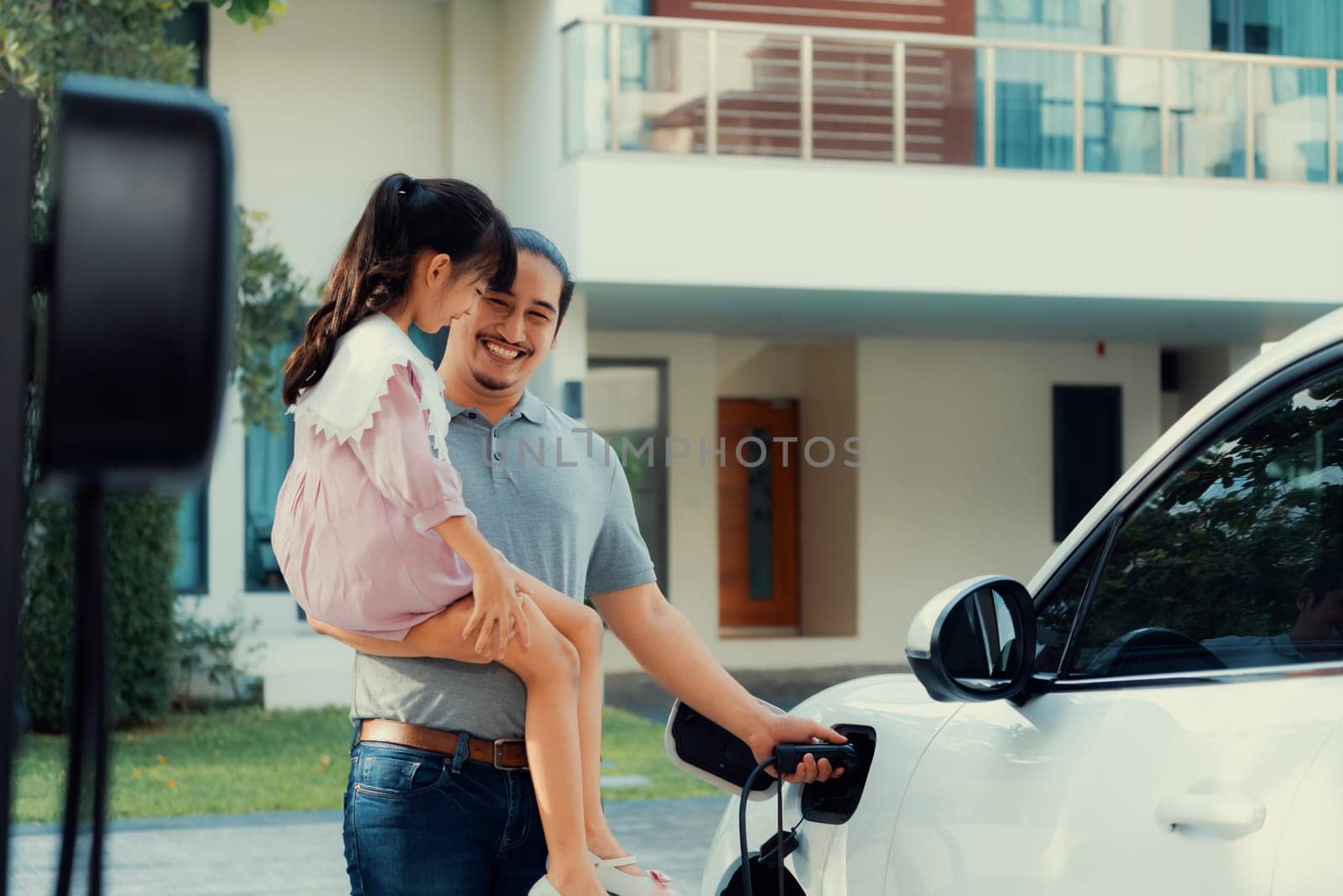 Progressive concept of father and daughter with EV car and home charging station by biancoblue