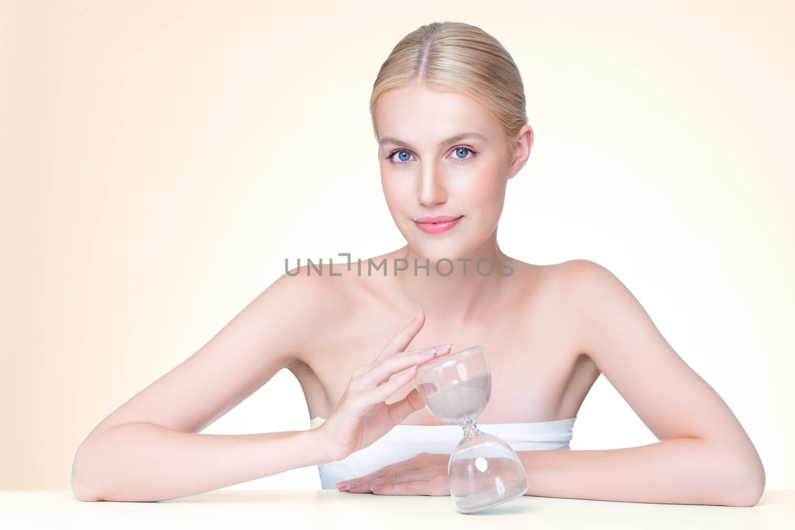 Personable model holding hourglass in beauty concept of anti-aging skincare treatment for woman. Young girl portrait with perfect smooth clean skin and flawless soft makeup in isolated background.