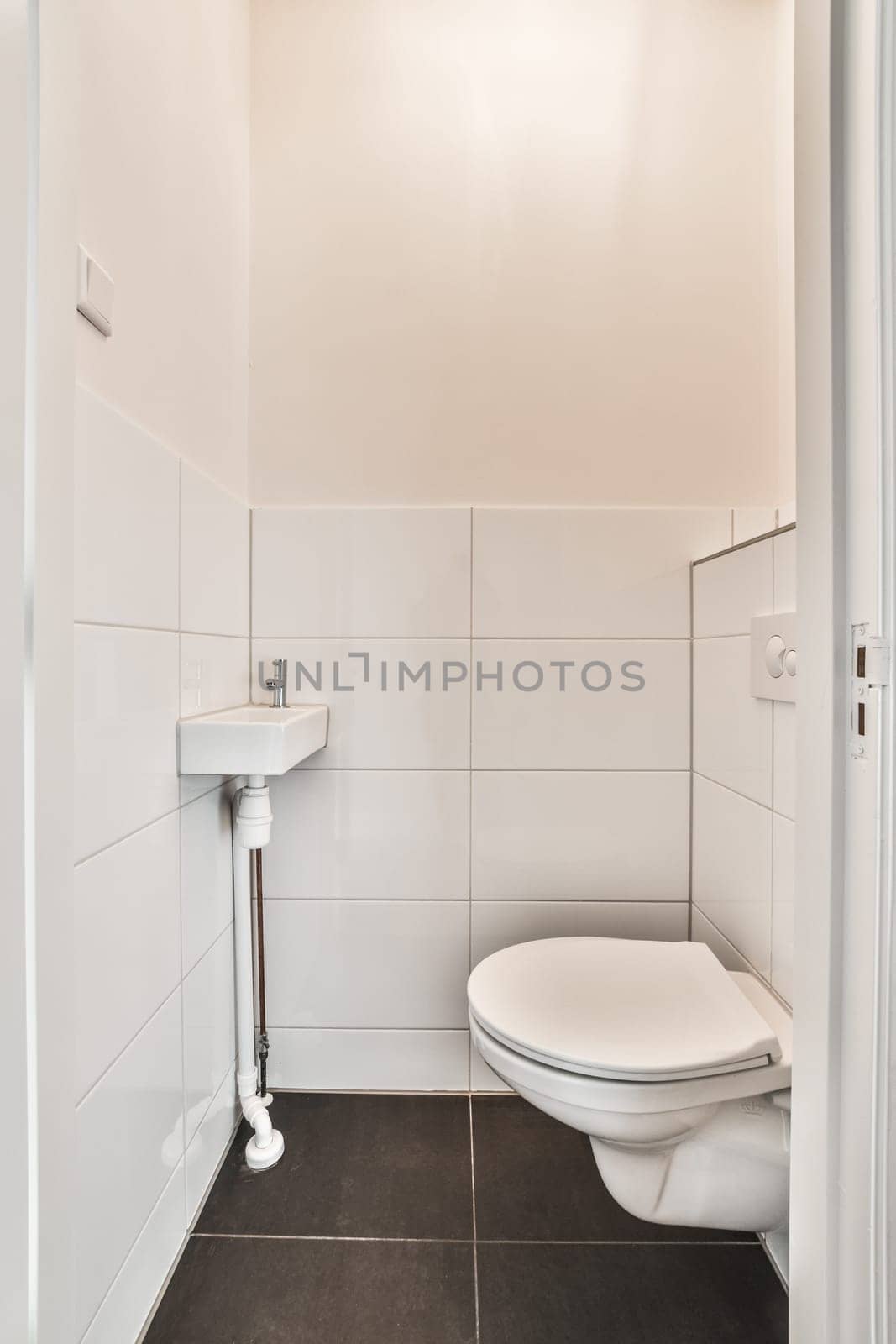 a white toilet in a bathroom with black tiles on the floor and wall behind it is an open shower stall