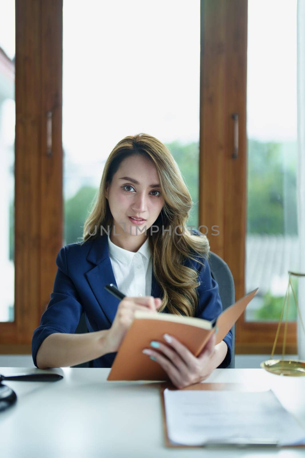 Portrait of a young Asian lawyer studying a lawsuit for a client using notebooks and paperwork on a desk.