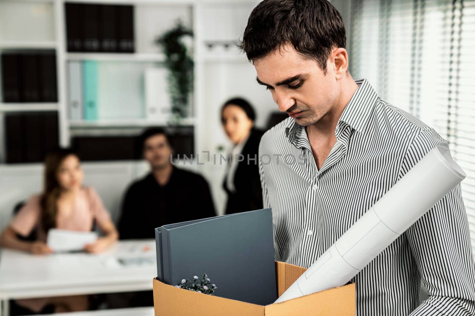Depressed and disappointed employee packing his belongings after being fired for not being competent. Gossiped by his colleagues behind his back. Layoff due to economic depression.