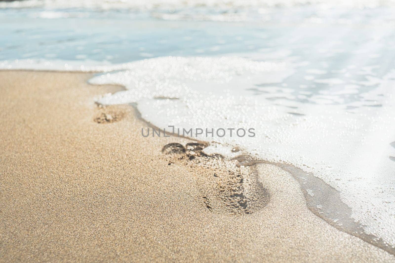 Footsteps and foam wave on the beach by the sea in summer