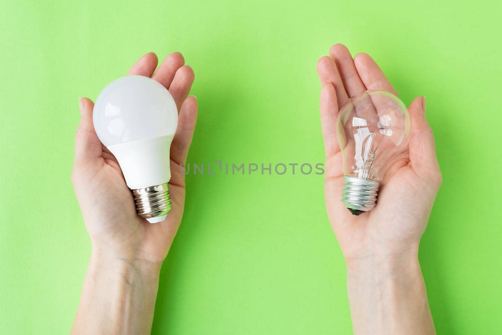 A set of two types of lamps, LED and incandescent, in the hands of a girl isolated on a green background. Energy-saving lamps