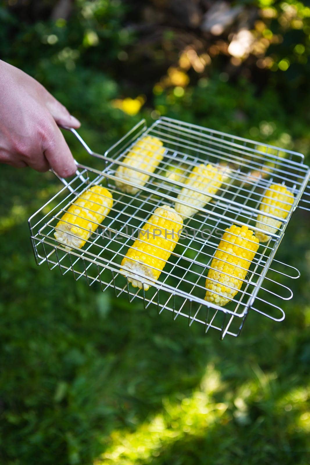 Delicious sweet corn is grilled on the grill. Outdoor recreation, close-up. Male hands are engaged in cooking