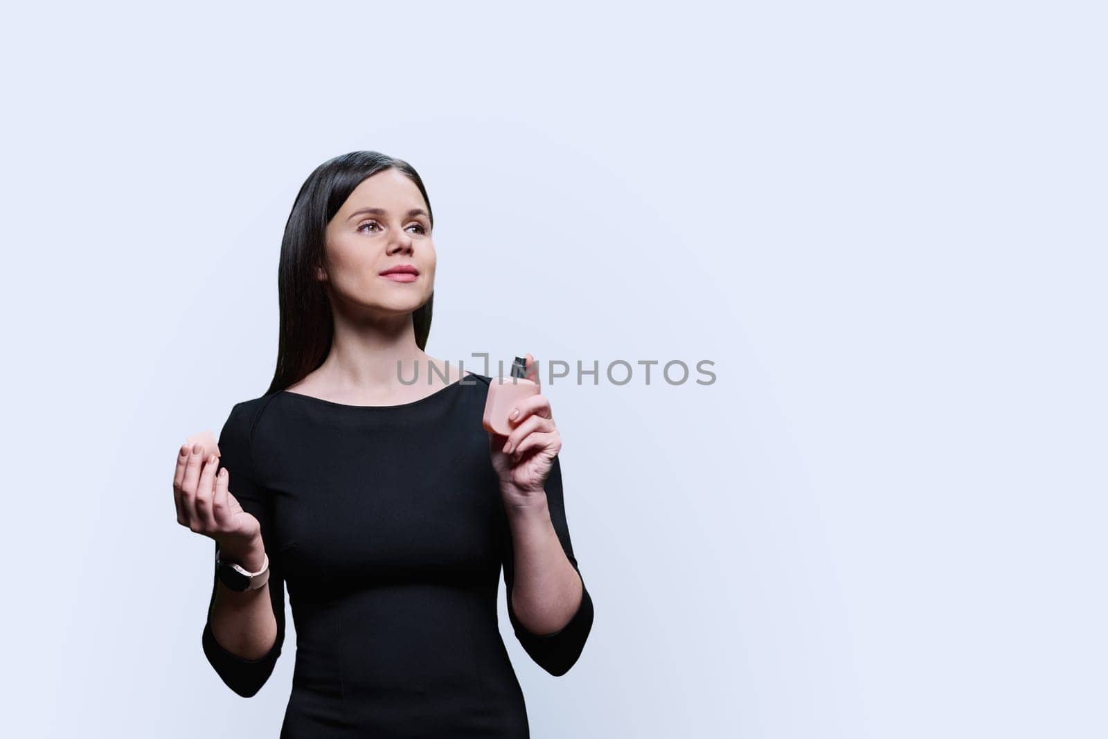 Young woman using bottle of perfume, on white studio background by VH-studio
