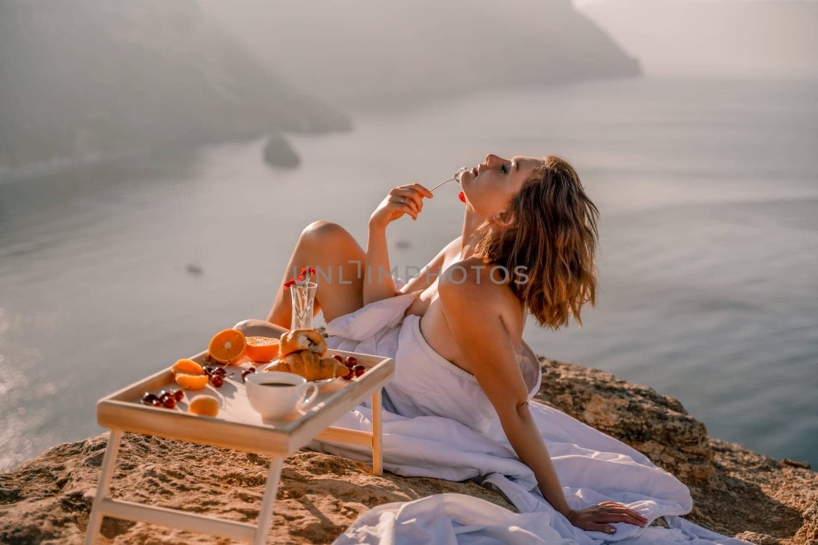 Woman wake up in bed wuth duvet and pillow over nature sea background outdoors. Back view. Good morning. Freedom concept