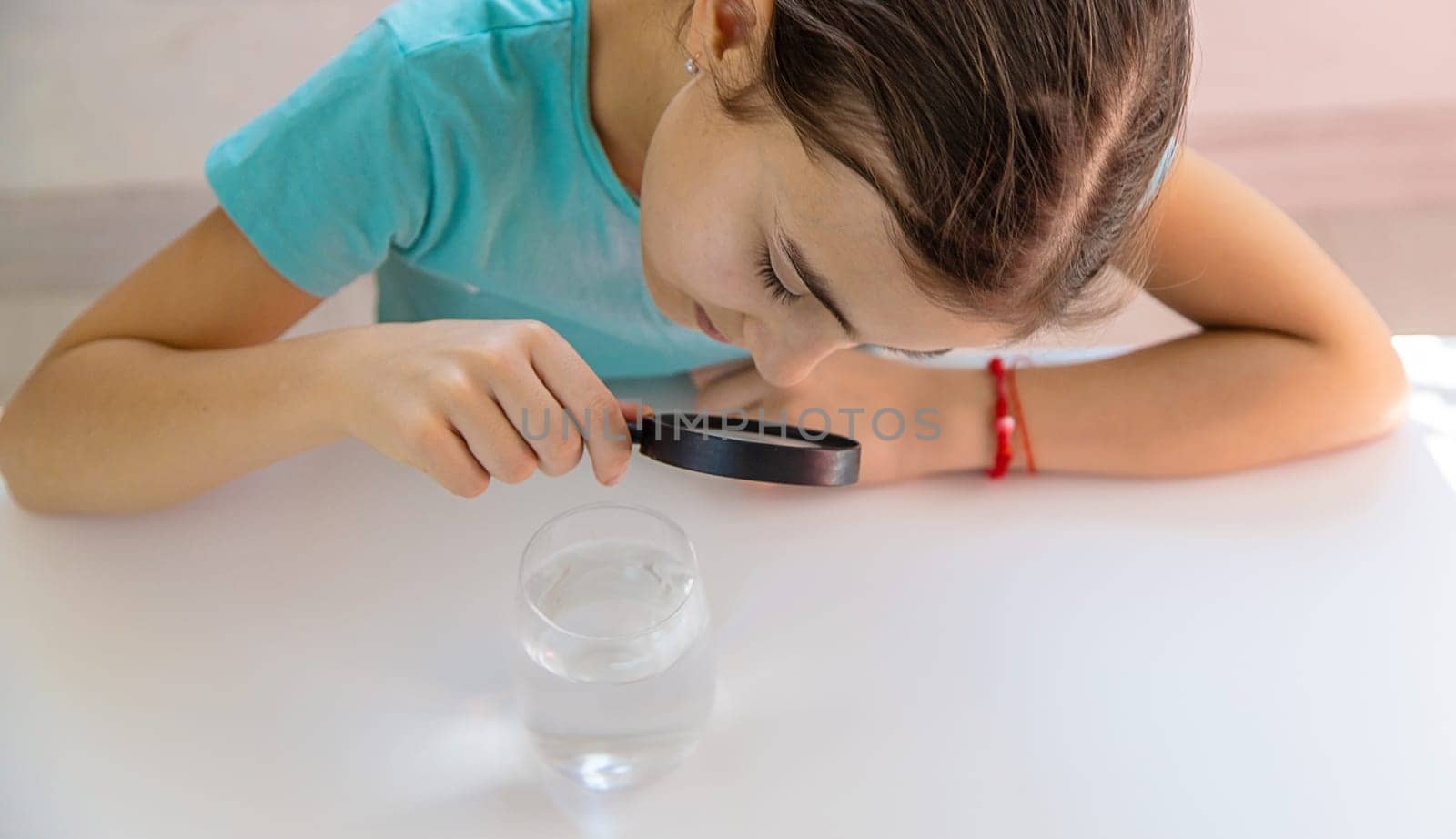 The child examines the water under a magnifying glass. Selective focus. Kid.