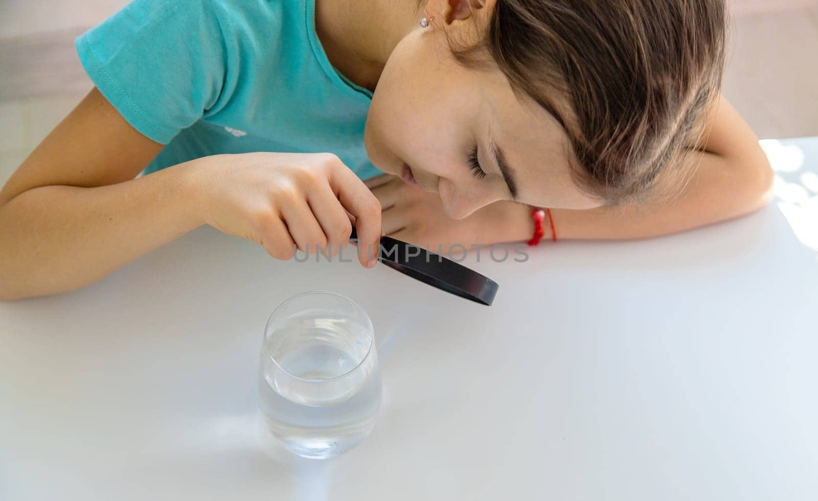 The child examines the water under a magnifying glass. Selective focus. Kid.