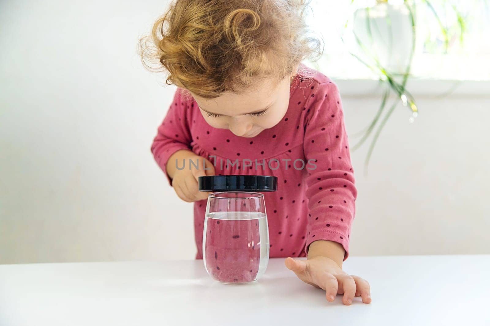 The child examines the water under a magnifying glass. Selective focus. Kid.