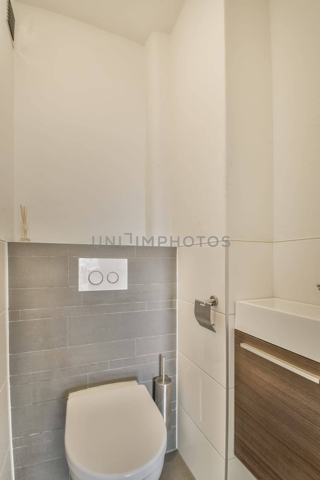 a modern bathroom with white walls and grey tiles on the wall, there is a toilet in the corner next to the sink