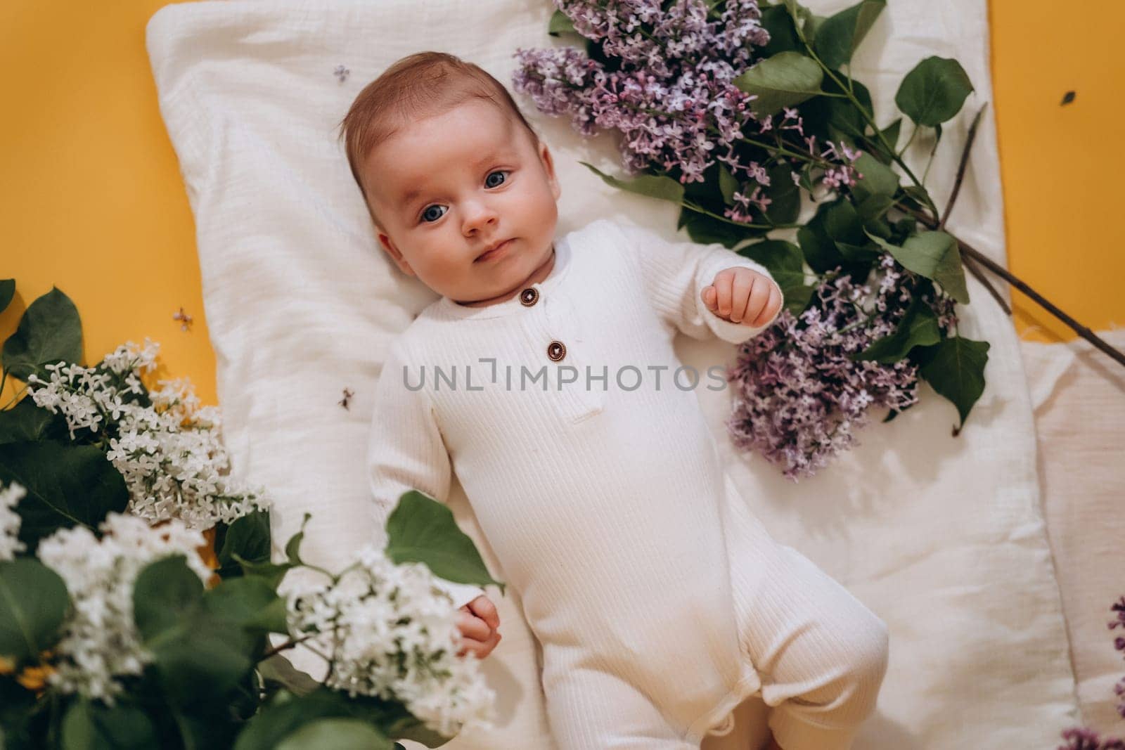 A cute baby is lying on a blanket among flowers. Spring concept. High quality photo