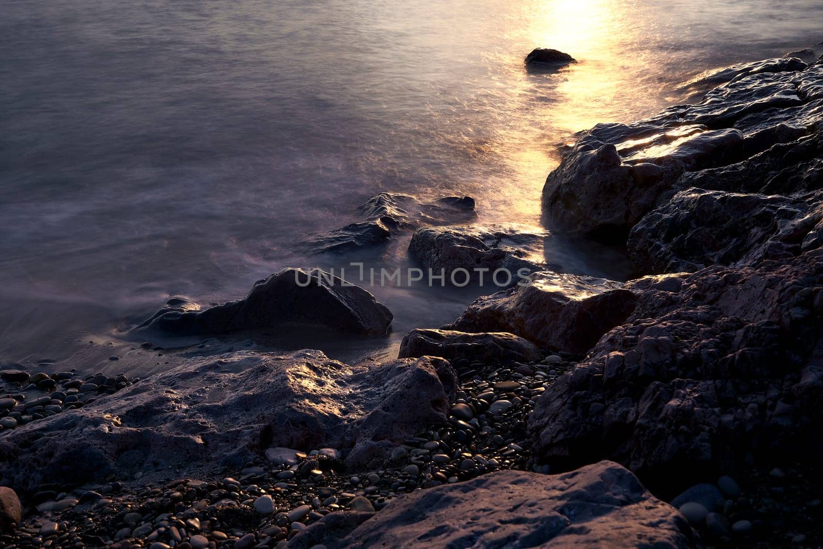 Line of stones from the coast at sunrise. Long exposure, silk effect water, big and small stones, sun rays, empty beach
