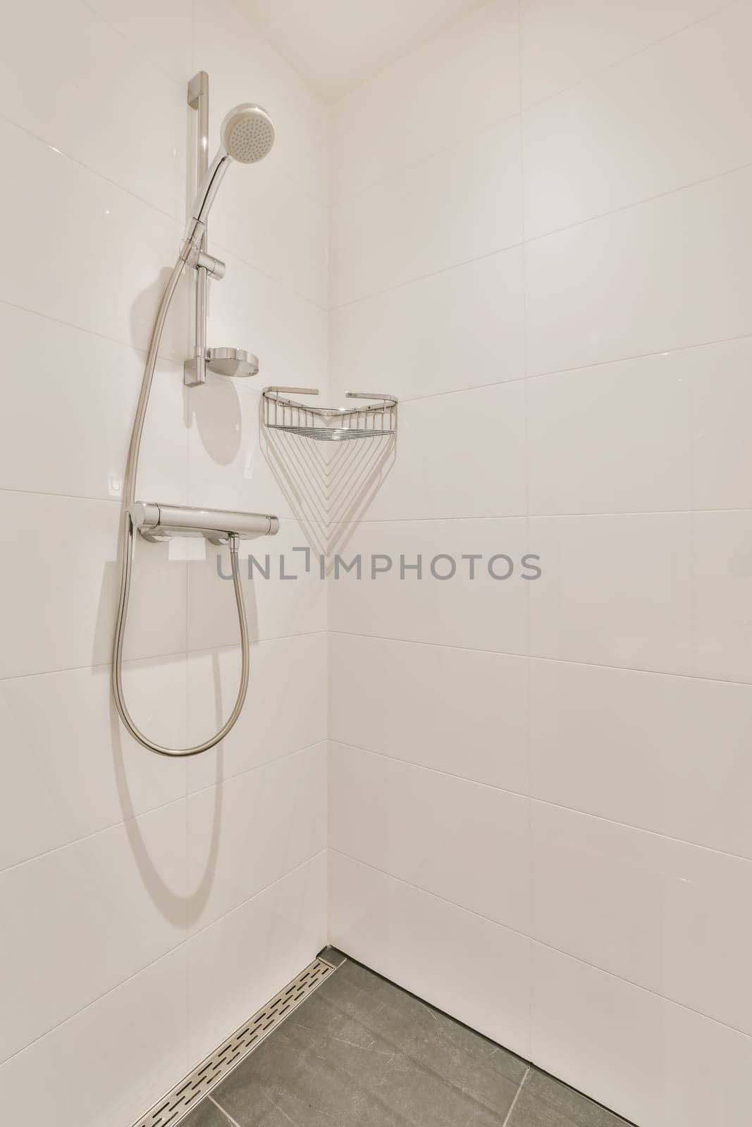 a shower in a white tiled bathroom with grey tile flooring and wall mounted handrails on the walls