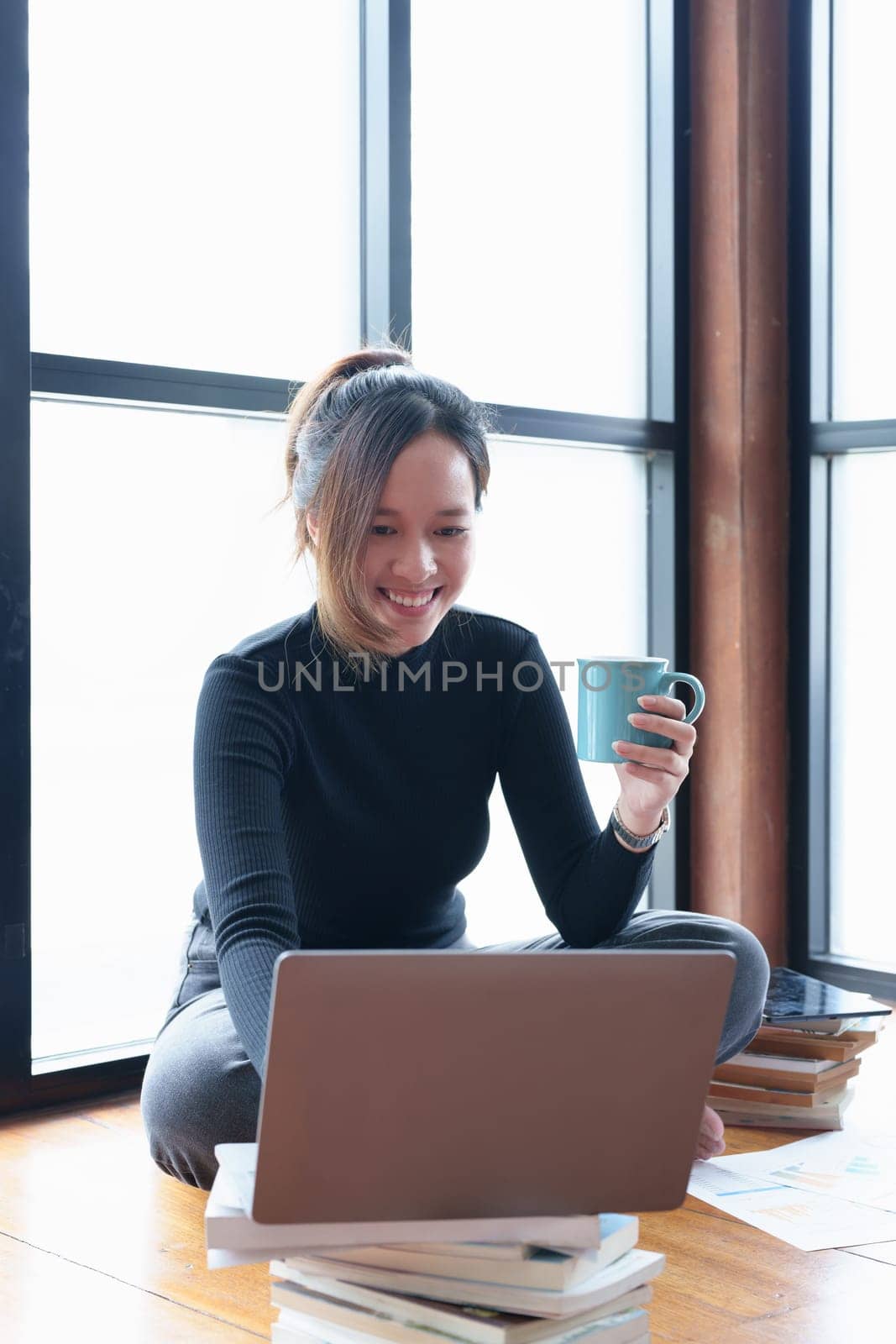 Portrait of an Asian woman using a computer to study online and drinking coffee while video conference by Manastrong